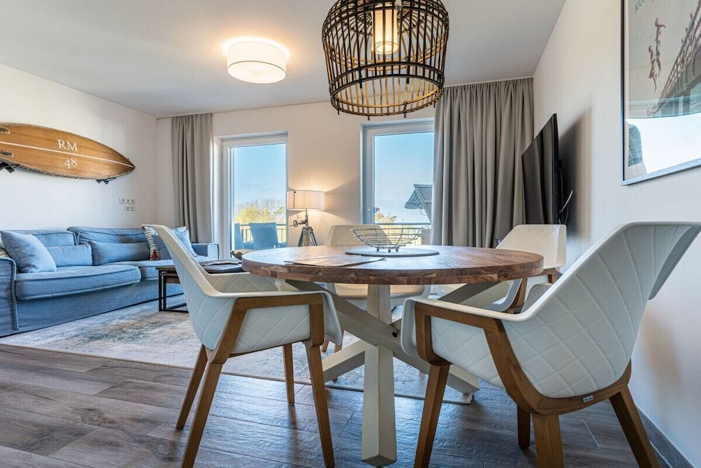 Una sala moderna con una mesa redonda de madera, sillas blancas con cojines, un sofá azul y una tabla de surf en la pared.