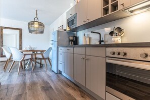 Eine moderne Küche mit grauen Schränken, einem eingebauten Ofen und einem Essbereich mit Holztisch und Stühlen.