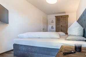 Une chambre à coucher avec un lit, une table de chevet avec une télécommande, un téléviseur fixé au mur et une porte.