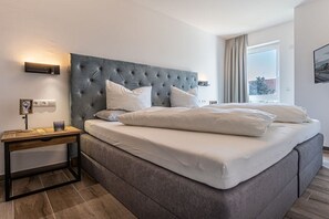 A hotel room with a large bed, a bedside table, a wall-mounted light, and a window with curtains. - Holiday apartment with 1 bedroom (Kühlungsborn)