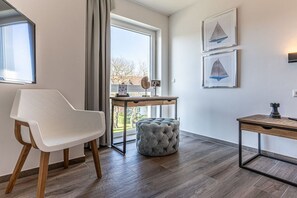 A modern room with a white chair, a round ottoman, a wooden desk, and two framed artworks on the wall. - Holiday apartment with 1 bedroom (Kühlungsborn)