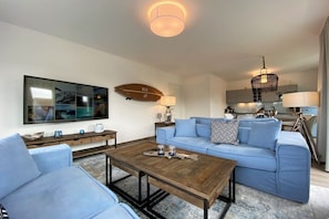 Ein modernes Wohnzimmer mit einem blauen Sofa, einem Holztisch und einem großen Flachbildfernseher an der Wand.