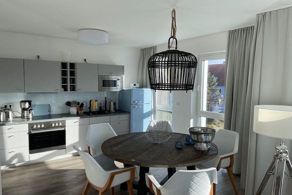 Eine moderne Küche mit weißen Schränken, einem blauen Kühlschrank und einem Essbereich mit Holztisch und weißen Stühlen.