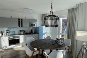 Una cucina moderna con mobili bianchi, un frigorifero blu e un'area pranzo con tavolo in legno e sedie bianche.