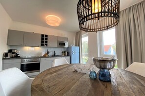 A modern kitchen with grey cabinets, a microwave, and a dining area with a round wooden table. - Holiday apartment with 1 bedroom (Kühlungsborn)