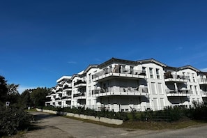 Un edificio residenziale a più piani con balconi, cielo sereno e vialetto lastricato.