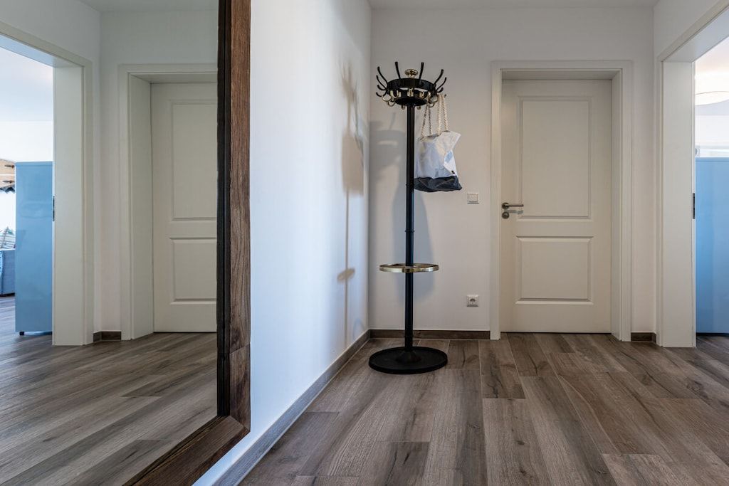 Un couloir au plancher de bois, un porte-manteau avec un sac, et deux portes blanches.