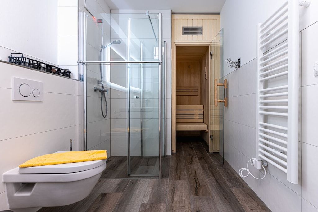 Un baño moderno con cabina de ducha de vidrio, inodoro y sauna de madera.