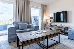 A modern living room with a sofa, a coffee table, a TV, and a balcony view. - Apartment Molli – Riviera Kühlungsborn 1 (Kühlungsborn)
