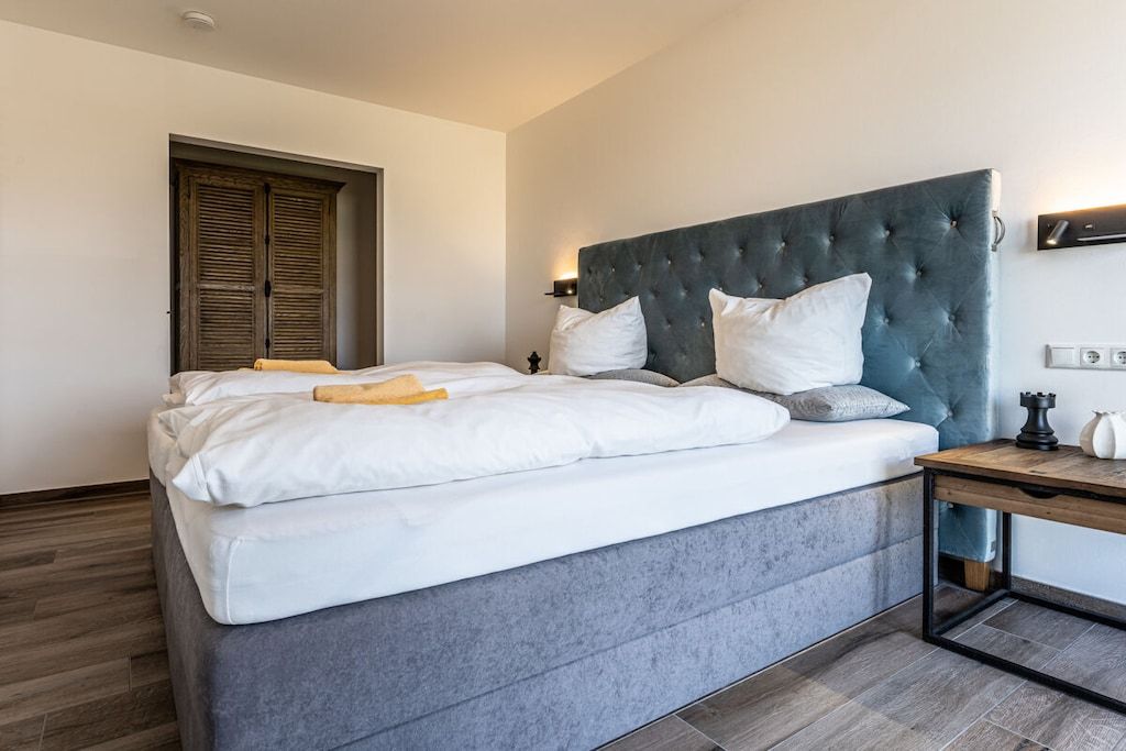 A modern bedroom with a large bed, a wooden nightstand, and a wardrobe.