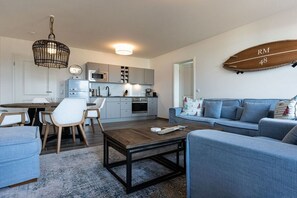 Una cocina moderna con armarios grises, un comedor con una mesa y sillas de madera, y una sala de estar con un sofá azul y una mesa de centro.