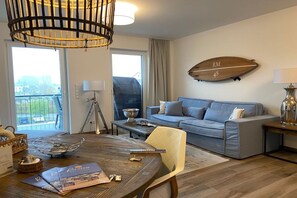 A living room with a sofa, a dining table, and a chandelier. - Holiday apartment with 1 bedroom (Kühlungsborn)