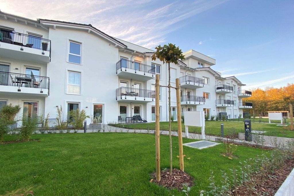 Un edificio residencial de varios pisos con balcones, un césped bien cuidado y un cielo despejado.