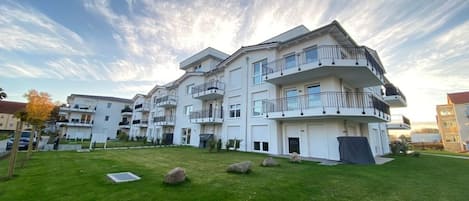 Un moderno edificio residencial de varios pisos con balcones, un césped cuidado y un cielo despejado.