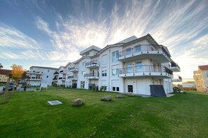 Un moderno edificio residenziale a più piani con balconi, un prato curato e un cielo sereno.