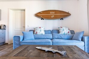 A living room with a blue sofa, two pillows with sailboat patterns, a wooden wall decoration with 'RM 48' text, and a model airplane on a coffee table. - Holiday apartment with 1 bedroom (Kühlungsborn)
