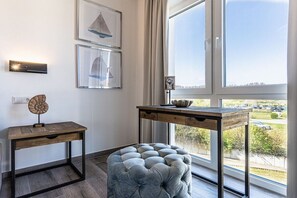 A room with a wooden table, a tufted ottoman, and framed artwork on the wall. - Holiday apartment with 1 bedroom (Kühlungsborn)