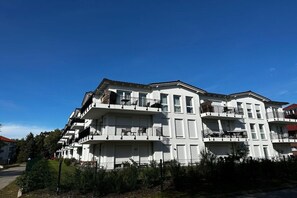 Un immeuble résidentiel à plusieurs étages, doté de balcons, avec un ciel bleu dégagé.