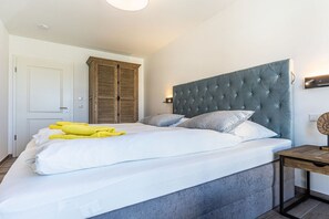 Une chambre à coucher avec un grand lit, une armoire en bois et une tête de lit recouverte d’un tissu gris.