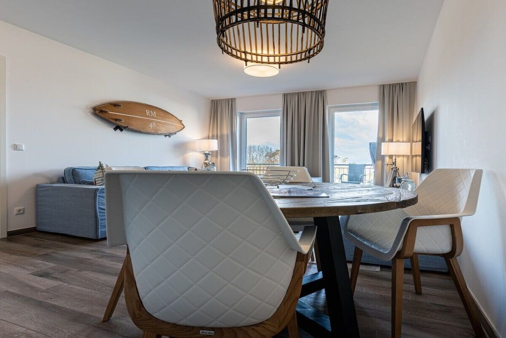 Un comedor moderno con una mesa redonda, dos sillas, una lámpara de techo de madera y un adorno de tabla de surf colgada en la pared.