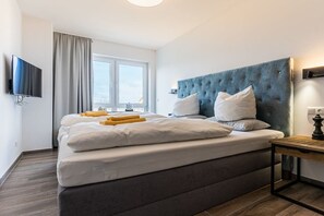 Ett modernt hotellrum med en stor säng, en platt-TV som är monterad på väggen, ett fönster med gardiner och ett sängbord med en lampa.