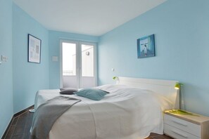 Een slaapkamer met een bed, nachtkastje en een raam met jaloezieën.
