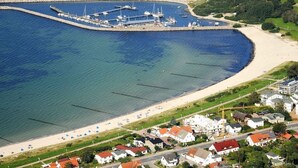 Ett flygbildsbild av ett kustnära område med en småbåtshamn, en strand och bostadshus.