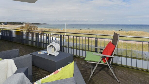 En balkong med utomhusmöbler, utsikt över stranden och ett räcke.