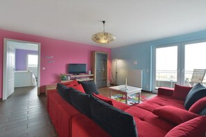 A living room with a red sofa, a television, and a small table. - Holiday apartment in Glowe with swimming pool (Glowe)