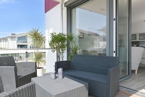 Ein Balkon mit Korbmöbeln, Topfpflanzen und einer Schiebetür zu einem Innenbereich.