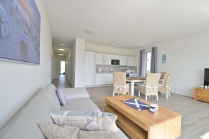 Een moderne woonkamer met een bank, een houten salontafel en een eethoek met stoelen.