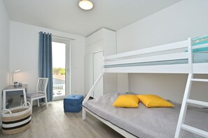 A bunk bed with a desk and chair, a window with curtains, and a small basket. - Holiday apartment in Glowe with swimming pool (Glowe)