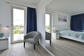 Een slaapkamer met een bed, een stoel, een nachtkastje en een raam met gordijnen.