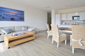 A modern living room with a sofa, chairs, a coffee table, and a painting of a beach scene. - Holiday apartment in Glowe with swimming pool (Glowe)
