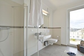 Een moderne badkamer met een glazen douchecabine, een wit wastafelmeubel en een toilet.