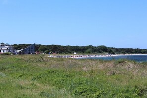 Een strand met een modern gebouw op de achtergrond, een heldere lucht en een grasveld vooraan.