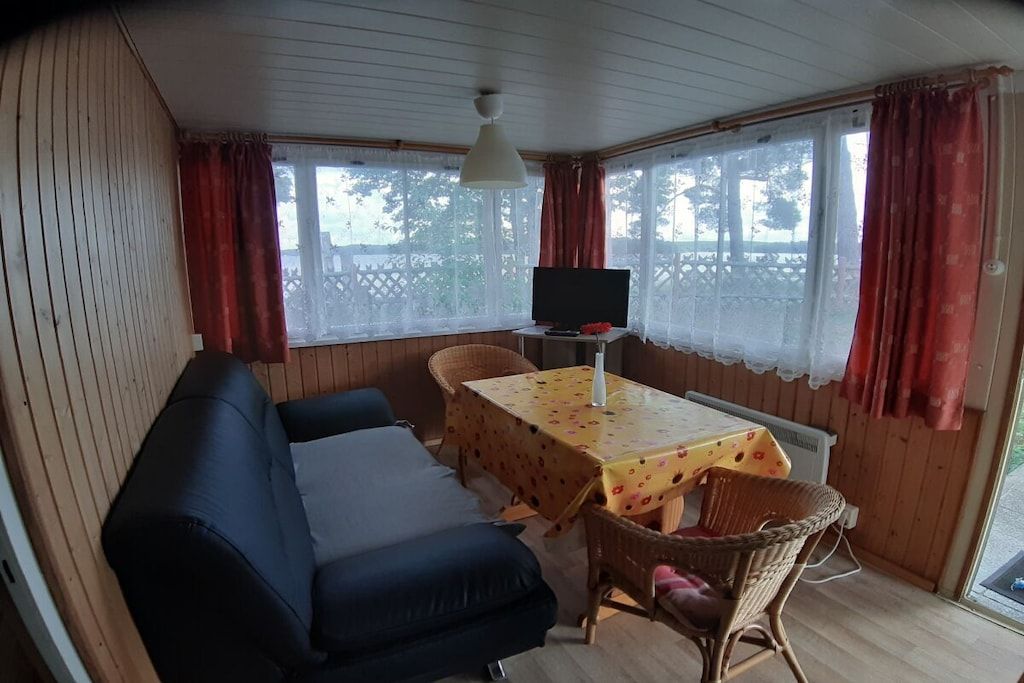 A room with a sofa, a table with a floral tablecloth, a television, and wicker chairs.