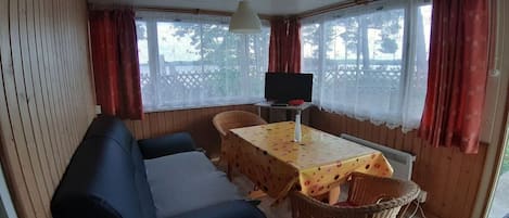 A room with a sofa, a table with a floral tablecloth, a television, and wicker chairs.