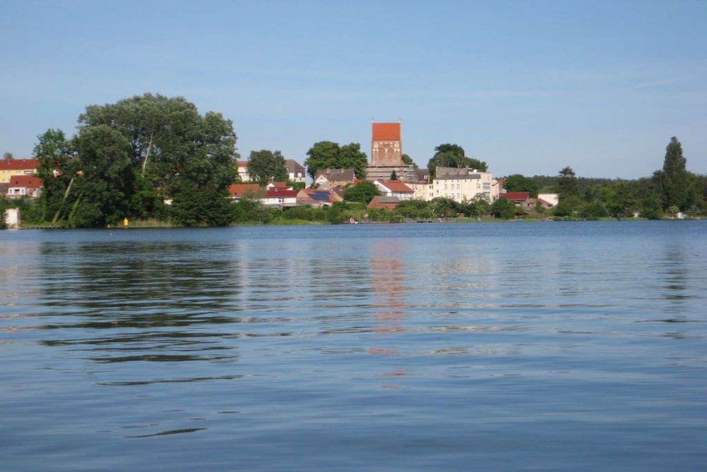 Un lago tranquilo con un pueblo al fondo, destacando una torre imponente y diversos edificios.
