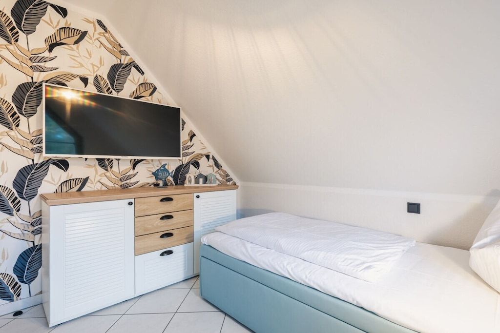 Ein Schlafzimmer mit einem Bett, einem an der Wand montierten Fernseher und einem Schrank mit Schubladen.