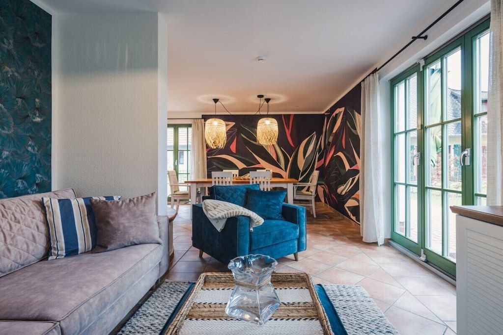 Ein Wohnzimmer mit einer Couch, einem blauen Sessel, einem Couchtisch und einer Wandmalerei.
