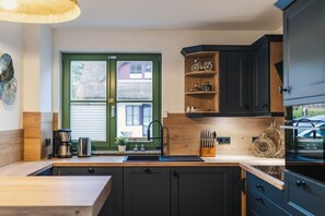 A modern kitchen with dark cabinets, a wooden countertop, and a window with a view of buildings. - Holiday home in Glowe with swimming pool (Glowe)