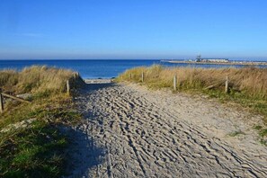 En sti af sand der fører hen til vand, med en bygning i det fjerne.