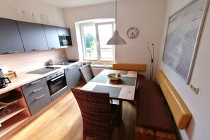 A modern kitchen with a dining area, including a bench, a table with a bowl of fruit, and a hanging light fixture. - Holiday apartment with 3 bedrooms (Kühlungsborn)