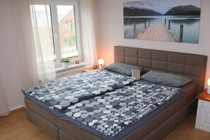 A bedroom with a bed, a window, a nightstand, and a painting on the wall. - Holiday apartment with 3 bedrooms (Kühlungsborn)