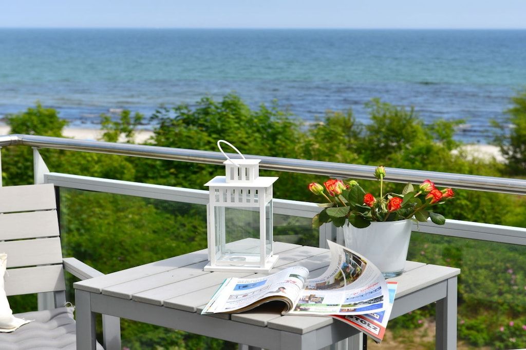A balcony with a white railing, a white lantern, a potted plant with red flowers, and a magazine.