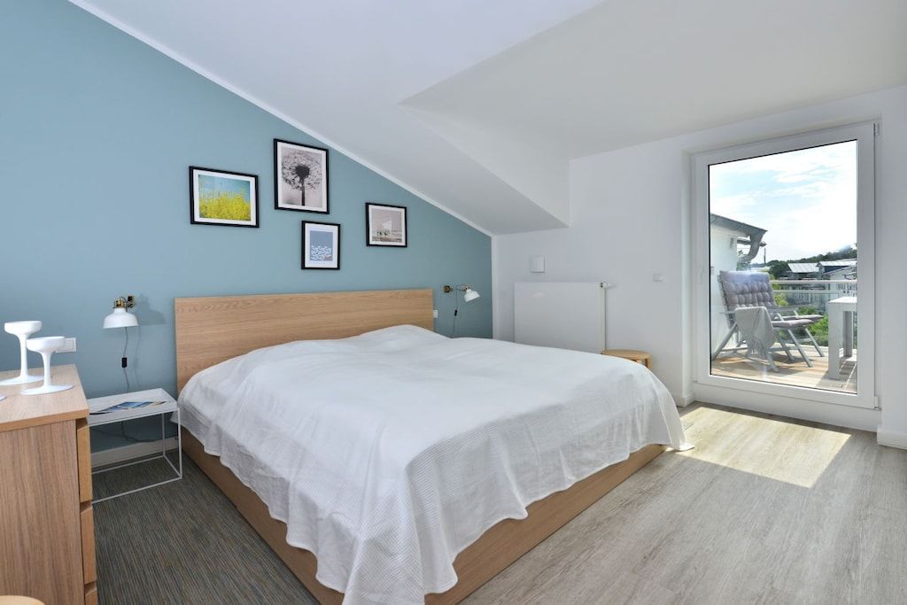 Een slaapkamer met een bed, een bureau en een stoel. Er hangen afbeeldingen in lijsten aan de muur.