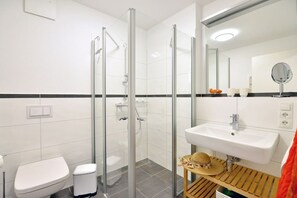 Een moderne badkamer met een douchecabine, een wit wastafeltje en een toilet.
