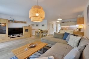 Een moderne woonkamer met een bank, salontafel, televisie en een eethoek.