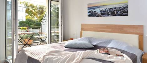 A bedroom with a bed, a nightstand, a painting, and a view through a glass door to an outdoor area.
